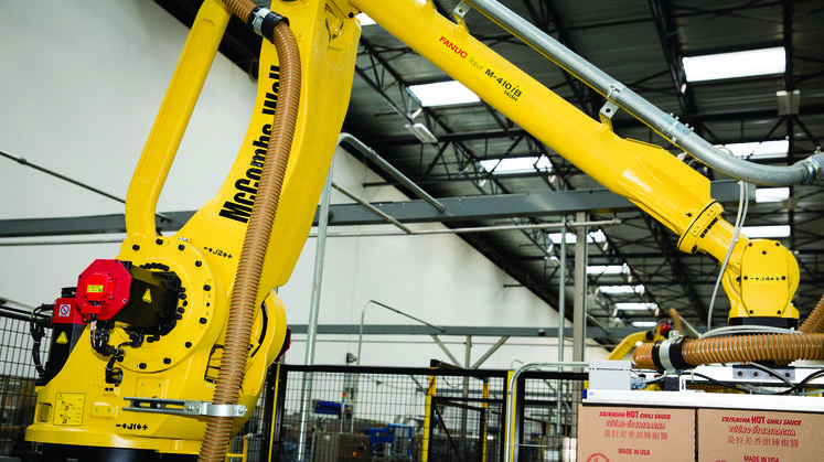 A Robotic Arm Moves Boxes of Sriracha Sauce