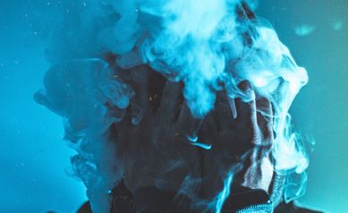 Man with cloud of smoke on his face and blue background, Vaping
