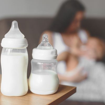 Bottles with breast milk on the background of mother holding in her hands and breastfeeding baby. Maternity and baby care.