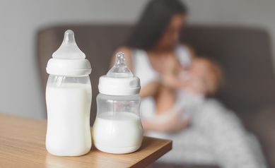 Bottles with breast milk on the background of mother holding in her hands and breastfeeding baby. Maternity and baby care.