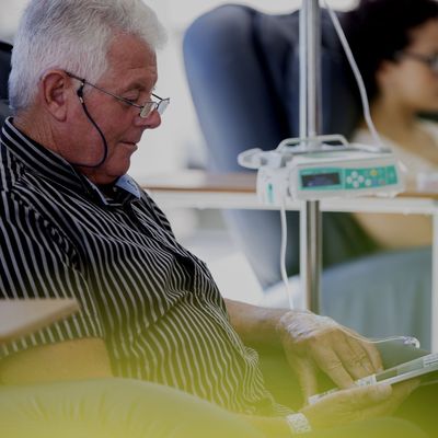 Senior patient receiving treatment while sitting and reading book in hospital ward