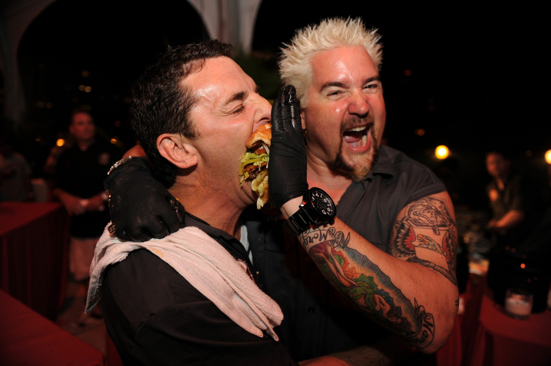 Guy Fieri gently feeds Carnival Cruise Lines' Senior Vice President of Guest Operations Mark Tamis a "Straight-up with a Pig Patty" burgerburger
